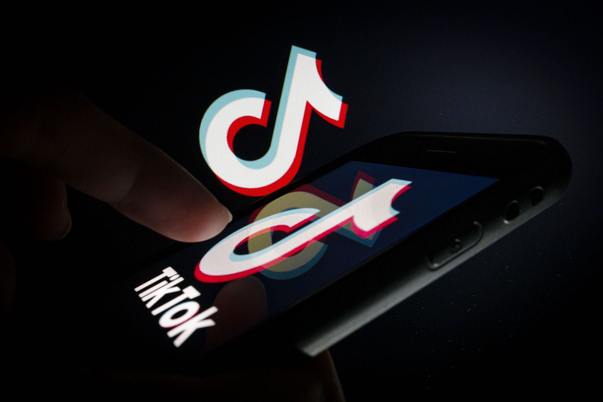 Логотип ТикТок в телефоне светится в темноте и на него направлен палец