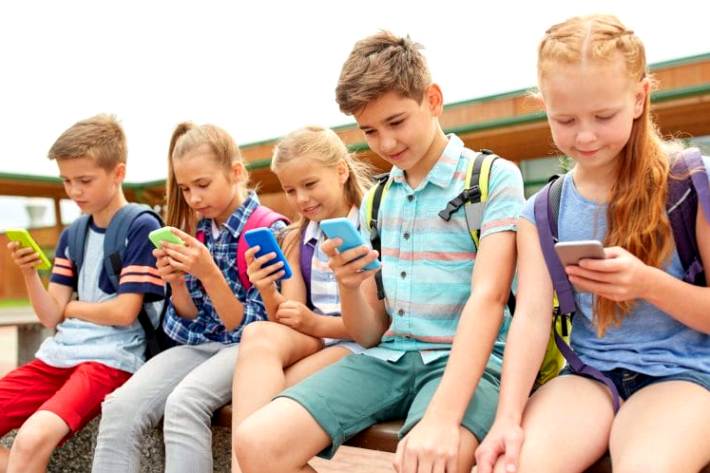 Дети младшего школьного возраста сидят и смотрят каждый в свой смартфон