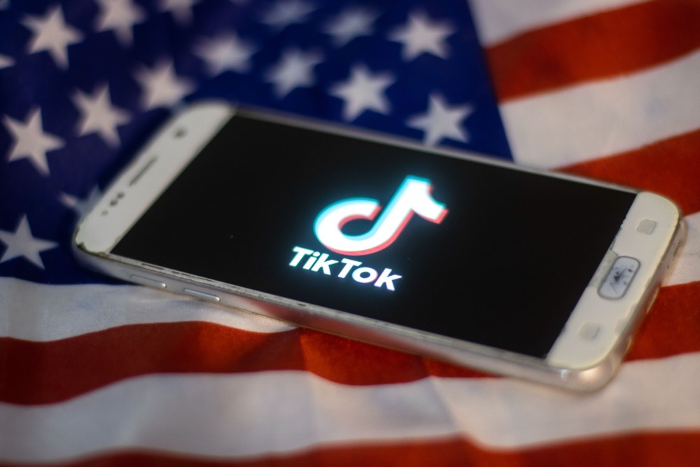 На флаге США лежит смартфон, на котором видно логотип ТикТок
