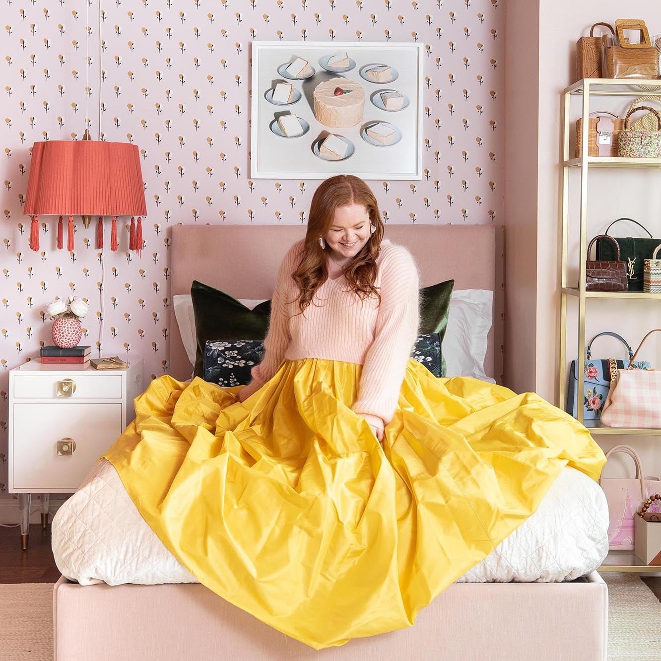 Девушка в бледно-розовой кофте и ярко-жёлтой юбке сидит в стильно оформленной квартире в розовых тонах