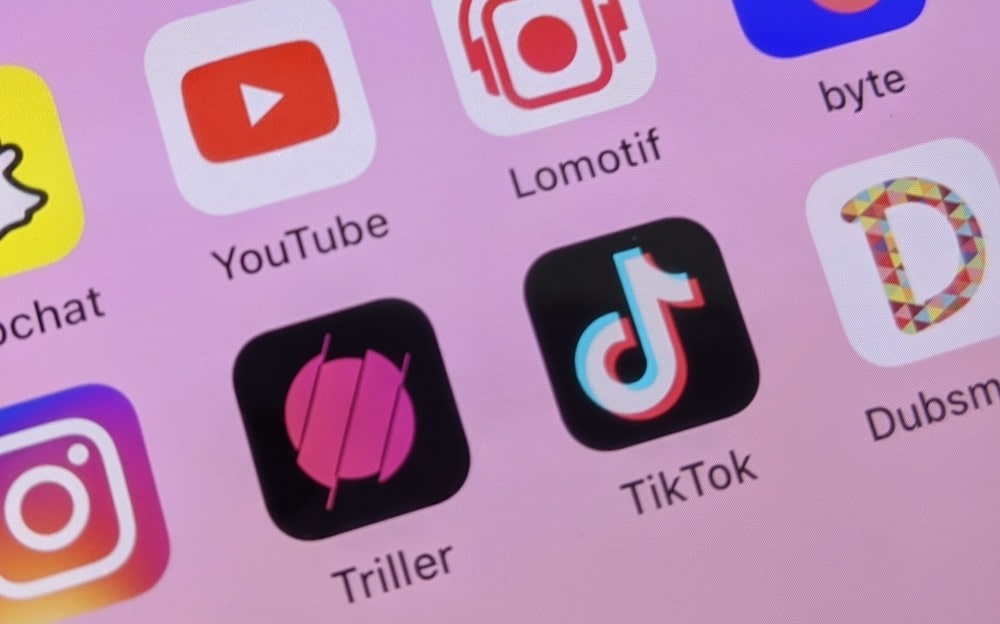 Иконки приложений на розовом экране смартфона, ТикТок на переднем плане