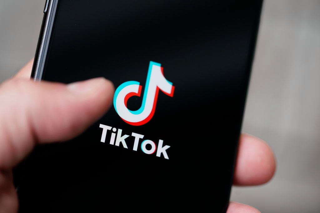 Рука держит смартфон с логотипом ТикТок на чёрном экране