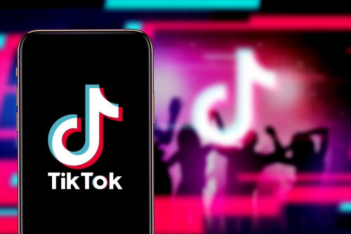 Смартфон с логотипом ТикТок на фоне разноцветных неоновых огней
