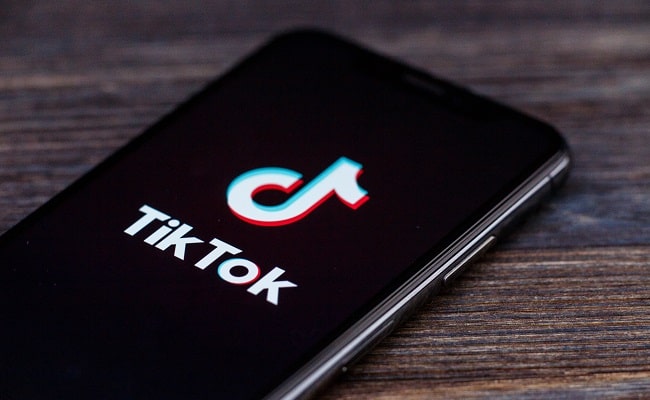Смартфон с логотипом ТикТок на экране лежит на деревянной поверхности