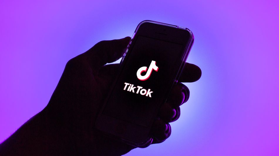 Рука на фиолетовом фоне держит телефон с лого ТикТока